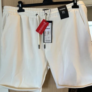 Vita shorts med snörning från Icono strl: XXL - Fräscha vita shorts från Icono i storlek XXL. De har elastisk midja med snörning, två sidofickor och två bakfickor. Perfekta för sommardagar, med en clean och enkel look. Materialet känns mjukt och bekvämt, och passformen är normal. Snygga att matcha med en t-shirt eller hoodie.