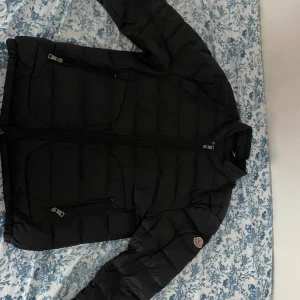 Svart Moncler jacka  - Säljer en svart dunjacka från Moncler med klassisk quiltad design och Moncler-logga på ärmen. Jackan har dragkedja framtill, flera fickor med dragkedja och hög krage. Perfekt för kalla dagar och riktigt snygg till dom flesta stilarna. Det går även att bytas mot andra prylar.