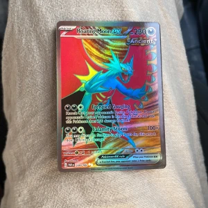 Roaring Moon ex - Cool och färgstark Pokémonkort med Roaring Moon ex! Perfekt för samlare och spelare som vill ha något unikt i sin samling. Kortet har holografisk yta och kraftfulla attacker – ett måste för alla Pokémon-fans.