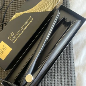 ghd Gold Professional Advanced Styler - Säljer en svart ghd Gold Professional Advanced Styler, en plattång med elegant och slimmad design. Kommer i originalförpackning med gulddetaljer. Perfekt för att skapa glansigt och rakt hår eller mjuka vågor. Ergonomiskt handtag och keramiska plattor för enkel styling.