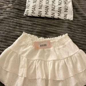 Vit volangkjol från Nelly XS - Supersöt vit kortkjol från Nelly med broderie anglaise och dubbla volanger. Kjolen har bred resår i midjan och är gjord i bomull med spetsdetaljer. Perfekt för dig som gillar romantisk och feminin stil. Helt slutsåld på hemsidan , nypris 300kr