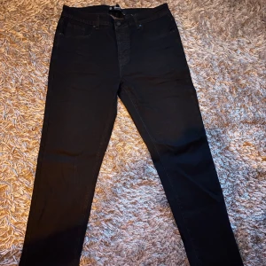 Svarta jeans från Brandit, W33 L32 - Svarta jeans från Brandit med raka ben. Jeansen har en stilren look med diskreta sömmar och svart patch bak i midjan. Jeansen är knappt använda och är i storlek W33 L32 blev ett spontan köpt som sedan inte passade mig.                                                                                    hör av vid frågor 