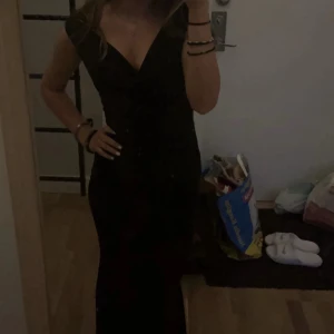 Svart långklänning med v-ringning - Snygg svart långklänning med djup v-ringning och korta ärmar. Klänningen har en figurnära passform som framhäver siluetten och är perfekt för dig som vill ha en elegant look. Materialet känns mjukt och följsamt mot kroppen. Använd en gång på min bal i nian (2022) och har inte kommit till användning sedan dess! 
