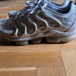 Nike Air Vapormax vita sneakers - Nike Air Vapormax sneakers i ljusgrått med ikonisk bubbelsula och vågformade detaljer på sidorna. Skorna har snörning och är tillverkade i syntet och textil. Perfekta för dig som gillar en futuristisk look och vill ha riktigt sköna sneakers.