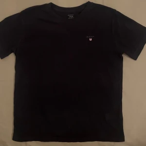 GANT T-shirt  - Svart T-shirt med Gant-logga framtill. Stilren och lätt att matcha. 