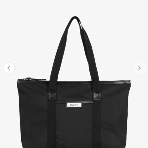 Svart shoppingväska från DAY ET - Stor svart shoppingväska från DAY ET med klassisk design och långa handtag. Väskan är tillverkad i slitstark syntet och har dragkedja upptill. Perfekt för att få plats med allt du behöver och enkel att bära över axeln.