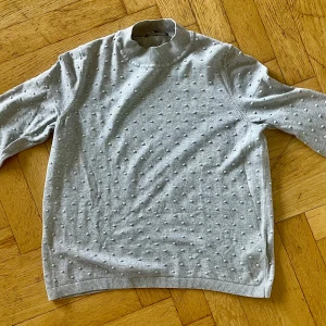 Grå  tröja Tommy Hilfiger - Snygg grå  tröja från Tommy Hilfiger i storlek XL men mer som L. Tröjan har coola prickiga detaljer över hela ytan och en ribbad högre krage. Perfekt för dig som gillar en stilren men ändå unik look. Liten broderad logga på ärmen för extra touch.