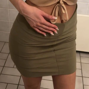 Olivgrön tight kjol  - Säljer en olivgrön tight kjol i kort modell. Kjolen har en enkel och stilren design med hög midja och stretchigt material som sitter snyggt på kroppen. Perfekt att matcha med crop top eller oversized hoodie för en trendig look. Passar s också