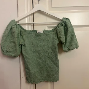 Grön offshoulder blus från Dobber - Söt ljusgrön offshoulder blus från Dobber med puffiga broderade ärmar och smockad kropp. Ärmarna har broderade blommor och toppen har en vågig kant nertill. Storlek S