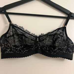 Svart spetsig bralette från Lounge - Supersnygg svart bralette från Lounge med blommig spets och tunna axelband. Modellen heter Desire Balcony. Aldrig använd och därför i nytt skick 