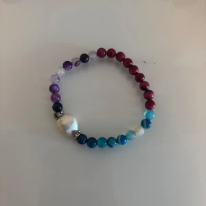 Färgglatt pärlarmband med stora pärlor - Unikt armband med runda pärlor i blått, lila, rött och vitt. En stor vit pärla är mittpunkten och ger extra wow-känsla. Perfekt accessoar för dig som gillar färg och vill sticka ut.