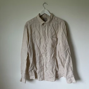 Beige linneskjorta från H&M, stl L - Snygg beige skjorta från H&M i 100% linne. Skjortan har klassisk krage, bröstficka och knäppning framtill. Regular fit med långa ärmar, perfekt för en chill och stilren look. Passar dig som gillar naturliga material och enkel design. Artnr: A333