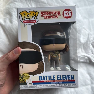 Battle Eleven #826 - Cool Funko Pop! figur från Stranger Things – Battle Eleven. Perfekt för fans av serien som vill ha en unik samlarpryl. Eleven har sitt ikoniska utseende med ögonbindel och blodig näsa. En grym present eller dekoration för alla som älskar popkultur och Netflix-serier! Pris kan diskuteras!