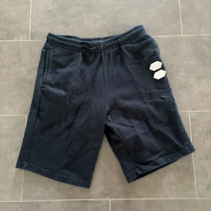 Svarta Off-White shorts i bomull - Snygga svarta shorts från Off-White med elastisk midja och två sidofickor. Mjukt bomullsmaterial och coola logodetaljer framtill och baktill. Perfekta för chill dagar eller streetwear-stil.