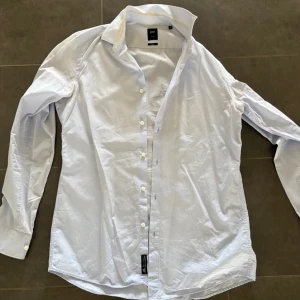Skjorta Hugo Boss  - Klassisk ljusblå skjorta från Hugo Boss med lång ärm och knappar framtill. Skjortan har en stilren design med krage och är tillverkad i bomull, perfekt för en clean och fräsch look.