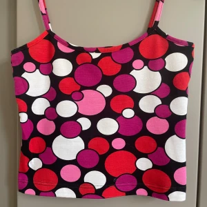 Färgglad prickig linnetopp - Säljer en superfin linnetopp med smala axelband och färgglatt prickigt mönster i rött, rosa, lila och vitt på svart botten. Toppen är i mjuk bomull med lite stretch för skön passform. Perfekt för dig som gillar retrovibbar och vill sticka ut i mängden!