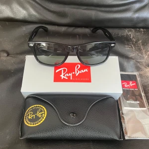 Svarta Ray-Ban Wayfarer solglasögon - Klassiska svarta Ray-Ban Wayfarer RB2140 med snygg, tidlös design. Bågarna är i blank svart plast och har Ray-Ban-logga på sidan. Glasen är grönt tintade och ger 100% UV-skydd. Perfekta för dig som vill ha en ikonisk look.
