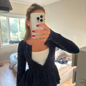 Mörkblå kofta med volangkant - Supersöt mörkblå kofta med knappar framtill och volangkant nedtill. Koftan har lång ärm och en feminin, lite utställd passform. Perfekt att slänga över ett linne eller t-shirt för en chill men ändå söt look.