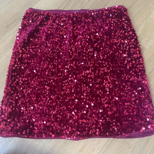 paljettkjol - Glittrig röd kortkjol från Lindex, täckt med paljetter som ger ett riktigt festligt intryck. Kjolen har en rak passform och elastisk midja för extra komfort. Perfekt för dig som vill sticka ut och glänsa lite extra.