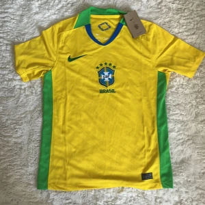 Brasilien fotbollströja Nike gul/grön S - Säljer en officiell Brasilien fotbollströja från Nike i storlek S. Tröjan är gul med gröna detaljer på sidor och krage, samt blå inslag vid halsen. Broderad CBF-logga och Nike Swoosh på bröstet. Tillverkad i 100% polyester med Dri-FIT-teknologi.
