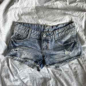 Blå lågmidjade jeansshorts med zebradetaljer - Snygga blå jeansshorts, låg midja, coola slitna detaljer och zebramönster vid fickorna. Köpta på second hand med prislappen kvar. Står inte storlek men skulle säga att passar en XS/S.