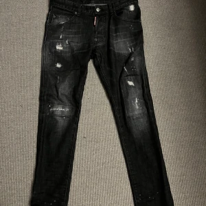 Svarta jeans från Dsquared2 - Säljer ett par svarta skinny/slim jeans från Dsquared2 med slitna detaljer och coola slitningar framtill och baktill. Jeansen har klassisk femficksdesign, låg midja och är tillverkade i stretchig bomullsdenim för en tight passform.