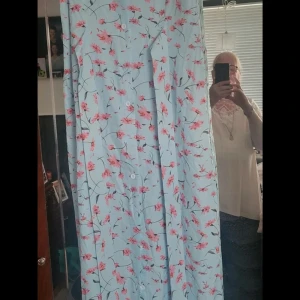 Ljusblå blommig långklänning med knappar - Superfin långklänning i ljusblått med rosa blommor och knappar framtill. Klänningen har ett luftigt fall och är perfekt för varma dagar. Söt och romantisk stil som verkligen sticker ut!