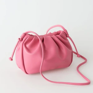 Rosa clutchväska med snörning - Snygg rosa axelväska i mjukt syntetmaterial med coola rynkade detaljer och justerbar axelrem. 