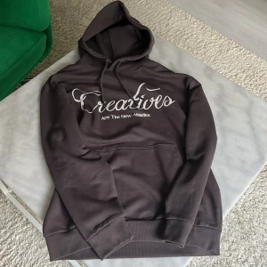 Brun hoodie från New Garments XS - Mörkbrun hoodie från New Garments i storlek XS men sitter som S, med vit text 'Creatives Are The New Athletes' på bröstet. Klassisk känguruficka, huva med snörning och mjukt bomullsmaterial. Perfekt för en chill stil, kan gå ner i pris vid snabb affär😊