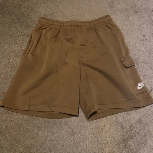 Bruna cargo shorts från Nike - Large - Ett par bruna Nike shorts med resår i midjan och en ficka på sidan. Använda ett gäng gånger (6-7 gånger), tvättade efteråt.