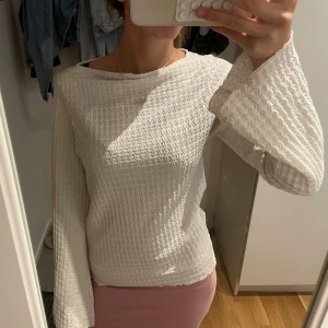 Vit långärmad topp med vida ärmar - Säljer en vit långärmad topp med vågigt strukturmönster och vida ärmar. Toppen har en avslappnad passform och är perfekt för dig som gillar unika detaljer. Materialet känns mjukt och lätt, och den höga halsringningen ger en stilren look.