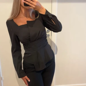 Svart blus - Snygg svart blus med unik fyrkantig ringning och markerad midja. Blusen är köpt i Paris och används vid två tillfällen!