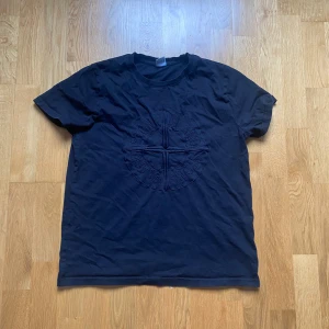 Svart Stone Island t-shirt med broderi - Svart t-shirt från Stone Island i bomull med stort broderat logomärke på bröstet. Klassisk rund hals och korta ärmar. Perfekt för dig som gillar streetwear och vill ha en clean look med en tydlig logga.