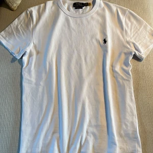 Vit t-shirt från Polo Ralph Lauren - Vit klassisk t-shirt från Polo Ralph Lauren med broderad marinblå logga på bröstet. Modellen är kortärmad och har rund halsringning. Tillverkad i mjuk bomull och har en normal passform. Perfekt för en clean och stilren look. Skick: 10/10, Fraktar inom 1 dag! Mvh