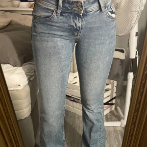 Blå bootcut jeans med broderade fickor - Säljer ett par ljusblå bootcut jeans med snygg brodyr på bakfickorna och klassisk femficksdesign från HM. Jeansen har normal passform.