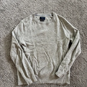 Grå stickad tröja från McNeal - En stilren grå stickad tröja från McNeal med cashmere feeling. Tröjan har rund halsringning, ribbade muddar och lång ärm. Perfekt för lager-på-lager och enkel att matcha med jeans eller chinos.