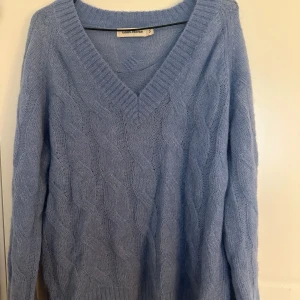 Ljusblå stickad tröja Carin Wester - Superfin ljusblå stickad tröja från Carin Wester med grovt kabelstickat mönster och djup v-ringning. 