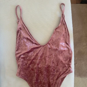 Rosa sammetsbody - Supersnygg rosa sammetsbikini med djup v-ringning och smala axelband. Materialet är glansigt och mjukt, vilket ger en lyxig känsla. Perfekt för dig som vill sticka ut på stranden i sommar!