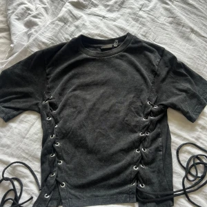 Svart t-shirt med snörning i sidorna - Cool svart t-shirt med snörning på sidor. Strl 32 men passar mig som har strl S. Se bild! Använd fåtal gånger och är i bra skick. 