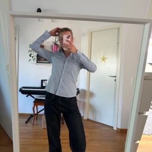 Ljusblå randig skjorta med knappar - Snygg ljusblå skjorta med tunna vita ränder och klassisk krage. Skjortan har lång ärm och stängs med knappar framtill. Perfekt för en clean och stilren look, passar till både jeans och kostymbyxor.