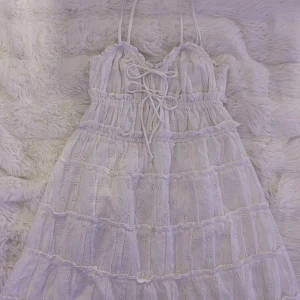 Vit sommar klänning från Gina Tricot - Supersöt vit kortklänning från Gina Tricot med tunna axelband, broderade blommor och volanger. Klänningen har snörning framtill och är gjord i luftig bomull, perfekt för varma dagar. Romantisk och trendig look! Bara använd 1 eller 2 gånger.