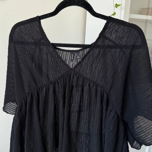 Svart transparent topp H&M - Svart topp från H&M i transparent, lätt och plisserat material. Klänningen har v-ringning, korta ärmar och en luftig, flowy passform. Perfekt för dig som gillar en stilren och edgy look.