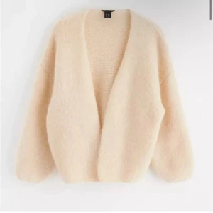 Beige fluffig kofta från Lindex - Supermjuk och fluffig beige kofta från Lindex med djup v-ringning och lång ärm. Koftan är stickad och har en oversized känsla, perfekt att slänga över ett linne. Snygg att stänga med brosch eller öppen för en chill look. Helt ny!  Upplevs som en S/M men är en M/L