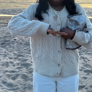 Kabelstickad kofta från Ralph Lauren - Kabelstickad kofta i mjuk, ljusbeige ull från Ralph Lauren. Klassisk modell med rund hals, ribbade muddar och knäppning framtill. Perfekt för lager-på-lager och snygg till både jeans och kjol.