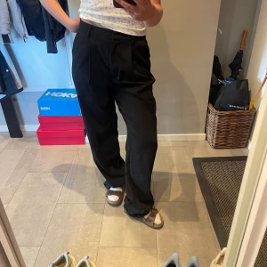 Svarta kostymbyxor med wide fit - Snygga svarta kostymbyxor med hög midja och raka, vida ben. Byxorna har pressveck framtill och diskreta fickor bak. Perfekta för en clean och stilren look. Materialet känns mjukt och följsamt, passar dig som gillar en relaxed men dressad vibe. Använda kanske 2 gånger. 