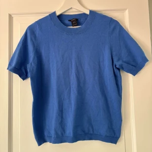 Blå kortärmad tröja från Lindex - En stilren blå tröja från Lindex i storlek S. Tröjan har korta ärmar, rund halsringning. Perfekt för dig som gillar enkel och clean stil med en pop av färg.
