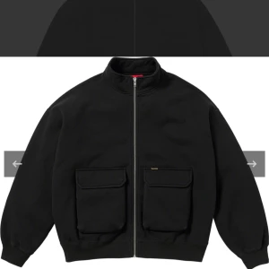 Supreme svart cargo zip sweatshirt - Supreme cargo pocket zip up sweatshirt i svart med två stora fickor framtill och hel YKK dragkedja. Jackan har hög krage och ribbade muddar. Tillverkad i bomull och har en clean streetwear-look med liten Supreme workwear logga på ena fickan. Skön och loose fit. Skicket är mycket bra. Man kan ha den som jacka också. Storlek L. Kvitto finns.