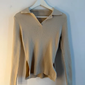 Beige ribbad tröja  - Säljer en beige ribbad tröja från SHEIN i storlek S. Tröjan har lång ärm, v-ringning med krage och är tillverkad i stretchigt material. Perfekt för lager-på-lager och har en clean, stilren look med slits i sidorna.
