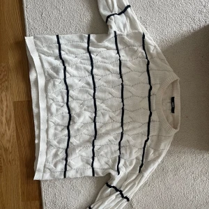 Vit stickad tröja med svarta ränder - Säljer en vit stickad tröja från H&M med svarta lodräta ränder och ett diskret kabelstickat mönster. Tröjan har rund halsringning och långa ärmar. Perfekt för dig som gillar en klassisk men trendig look.