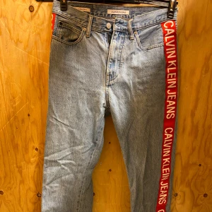 Calvin Klein ljusblå jeans med röd sida - Ljusblå jeans från Calvin Klein. Riktigt fina jeans som är i gott skick. Har nästan aldrig använts, förutom prislapp så är dem som nya. Priset är hugget i sten.